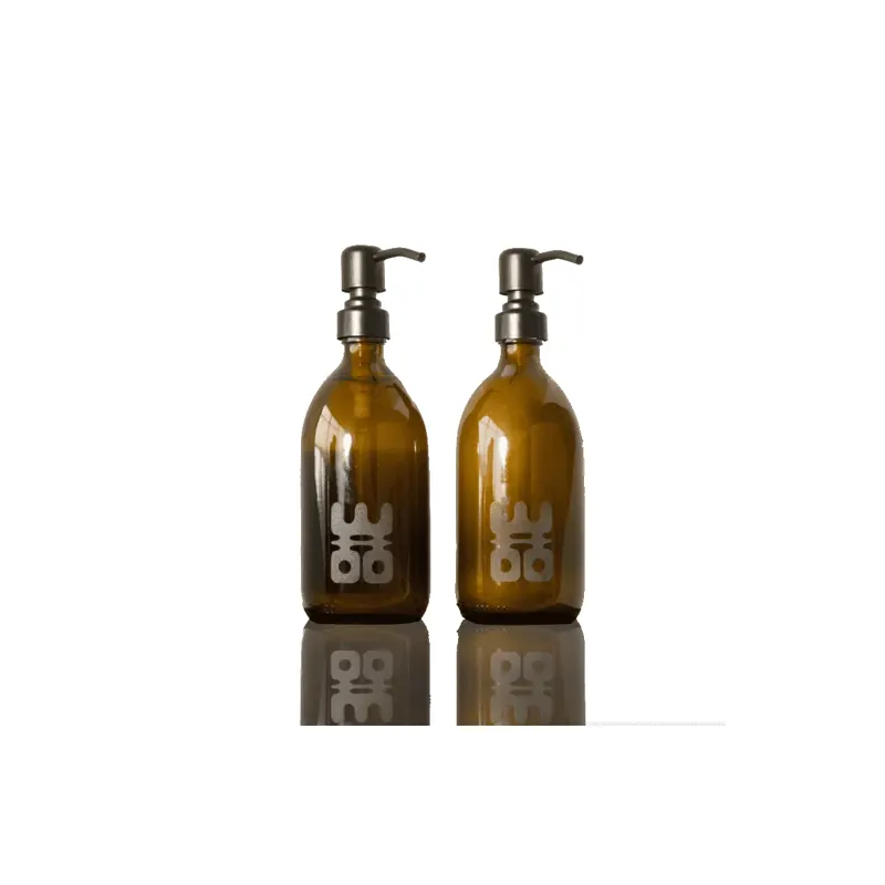 Twee amberkleurige glazen pompflessen met donkerkleurige pompen en het WOO-logo, naast elkaar op een groene achtergrond.